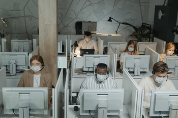 Call center- stanowiska biurowe, przy których siedzą pracownicy w słuchawkach. Mają na sobie maski.